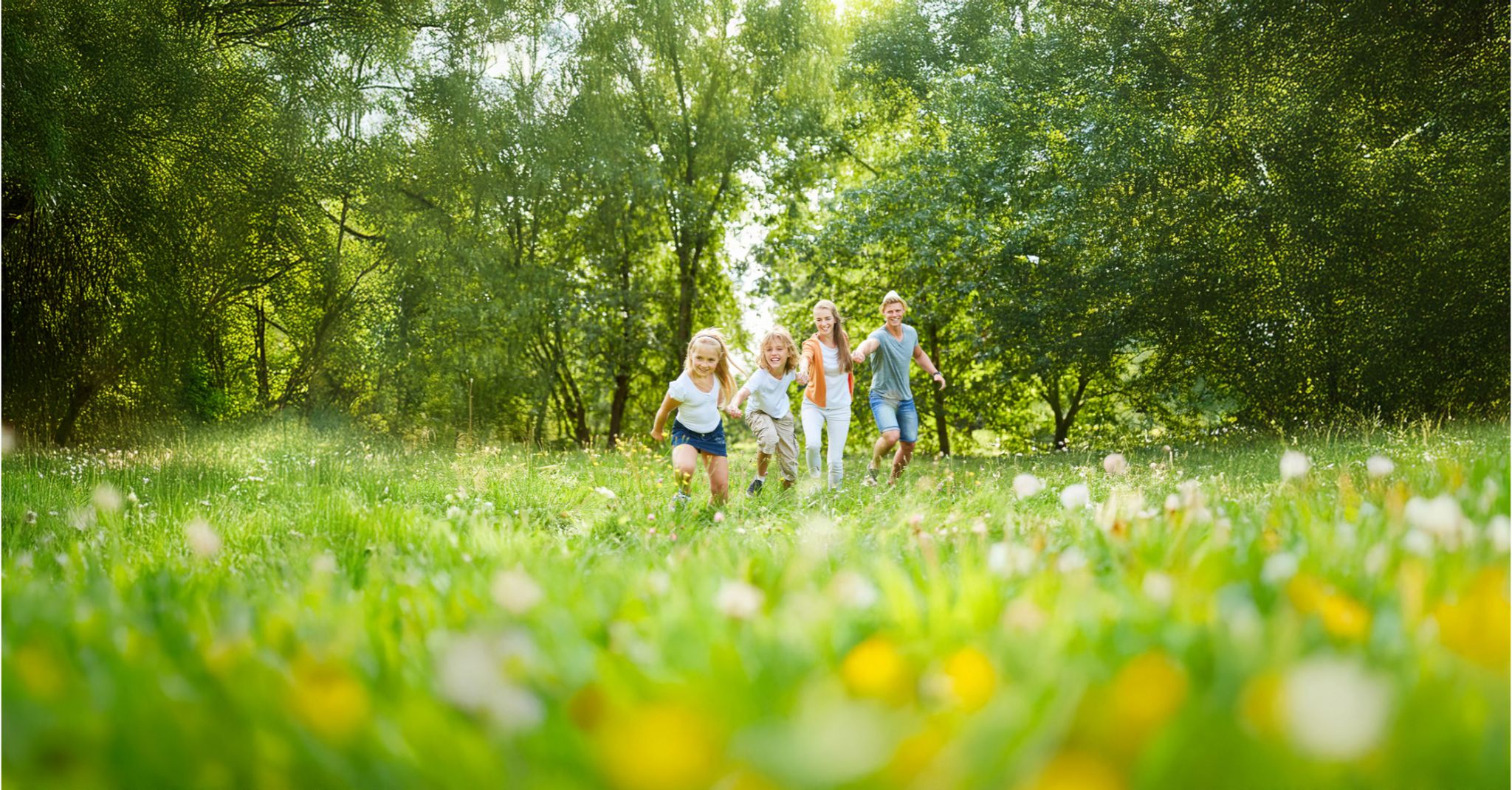 Familie läuft lachend zusammen über eine Wiese