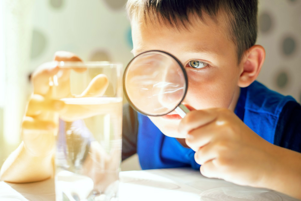 Kind hält Lupe vor ein Wasserglas
