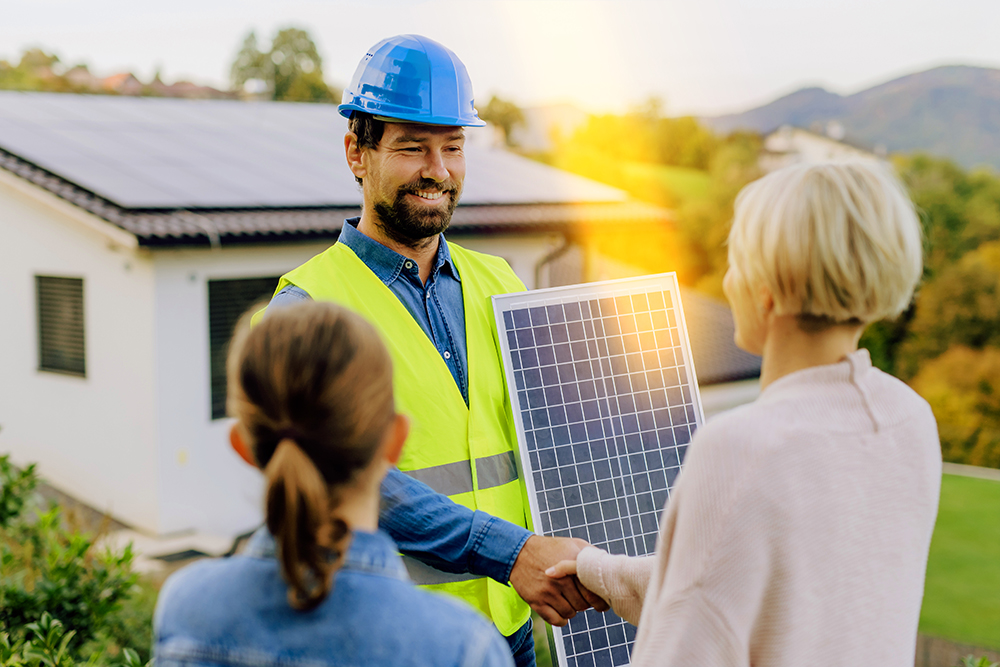 Installateur hält PV Modul und schüttelt einer Frau die Hand. 