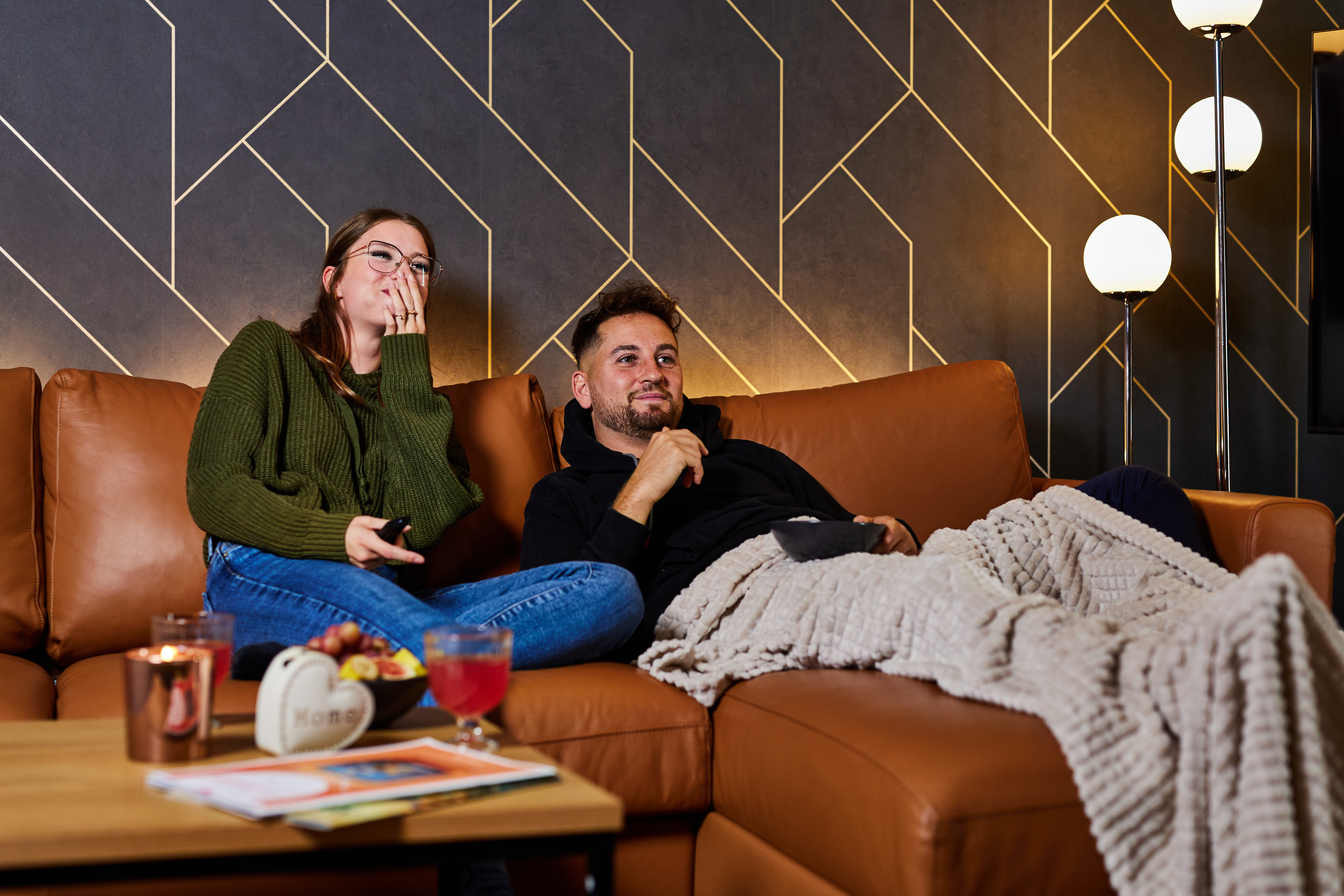 Paar sitzt auf einem Sofa und schaut amüsiert Fernsehen