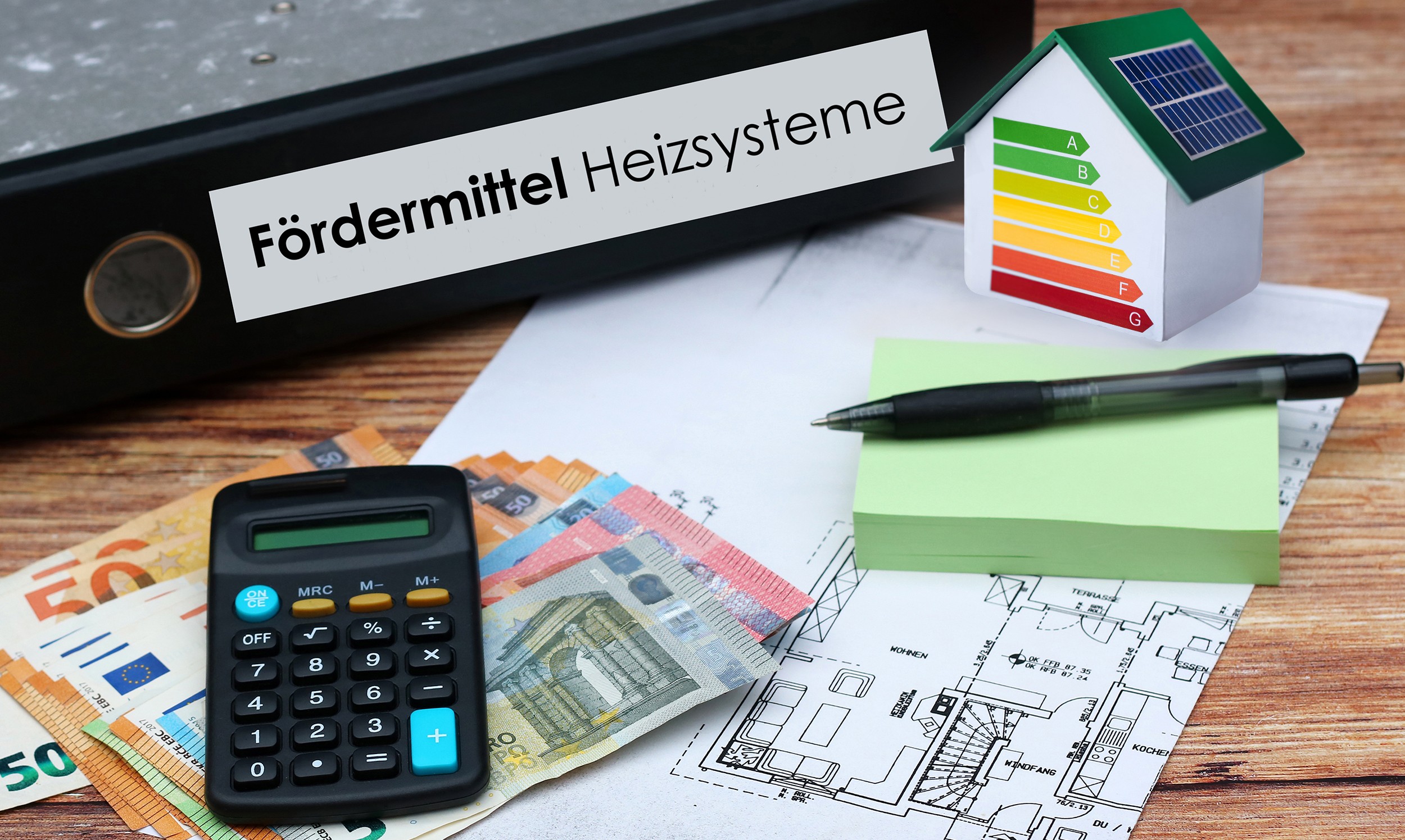 Euro-Geldscheine, Taschenrechner, Bauplan und Aktenordner mit dem Text "Fördermittel Heizsysteme" liegen auf einem Holztisch