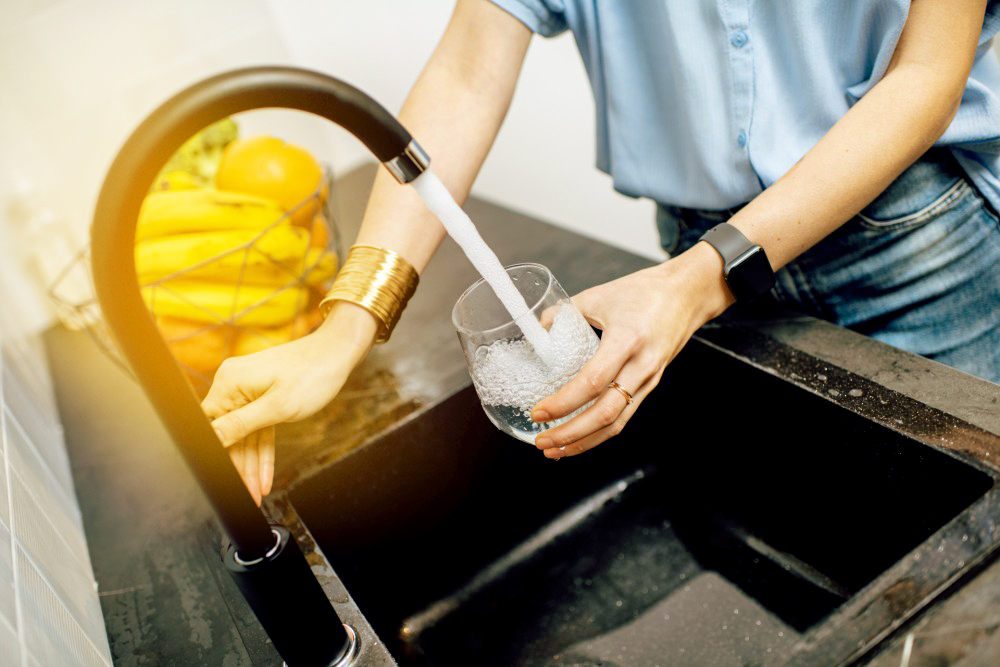 Frau füllt Glas mit Wasser am Wasserhahn