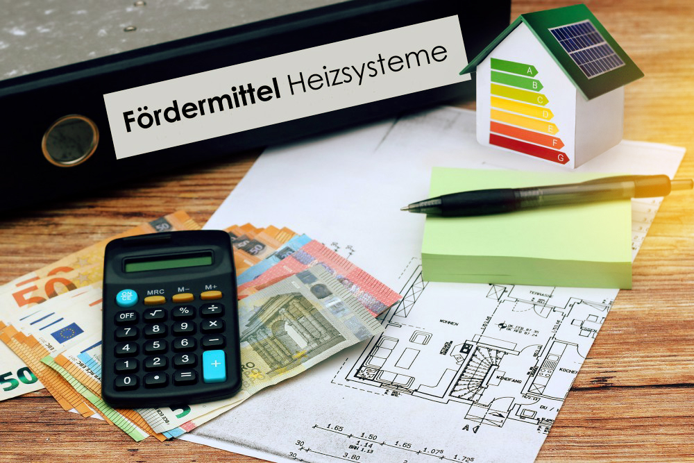 Euro-Geldscheine, Taschenrechner, Bauplan und Aktenordner mit dem Text "Fördermittel Heizsysteme" liegen auf einem Holztisch