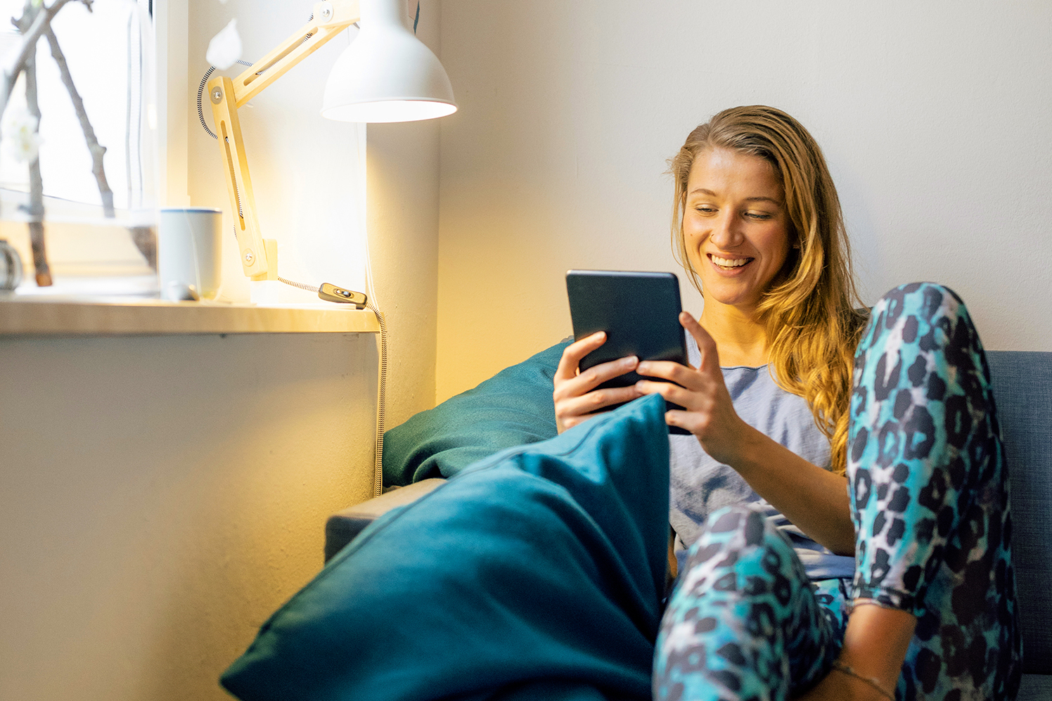 Frau sitzt mit E-Reader auf dem Sofa.