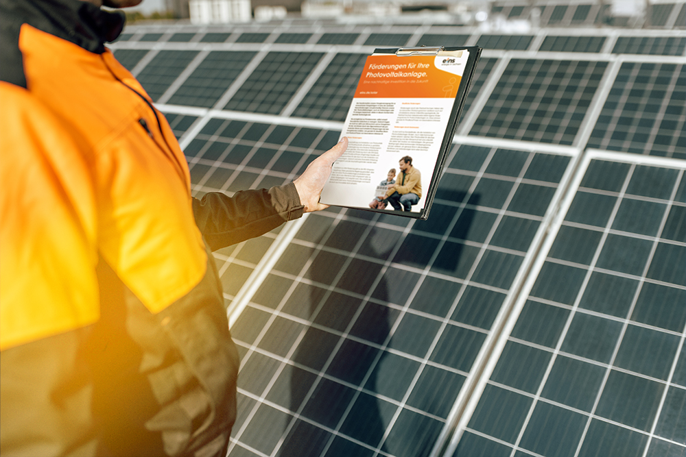 Mann in Arbeitskleidung steht vor Solarpanels und hält einen Solar-Förderantrag in der Hand