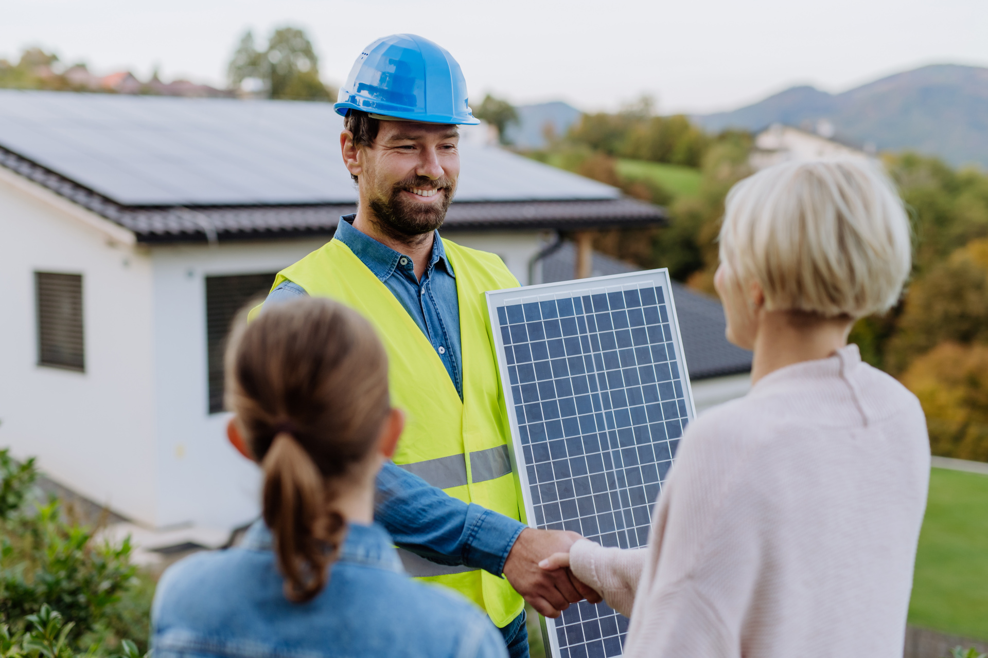 Installateur hält PV Modul und schüttelt einer Frau die Hand. 