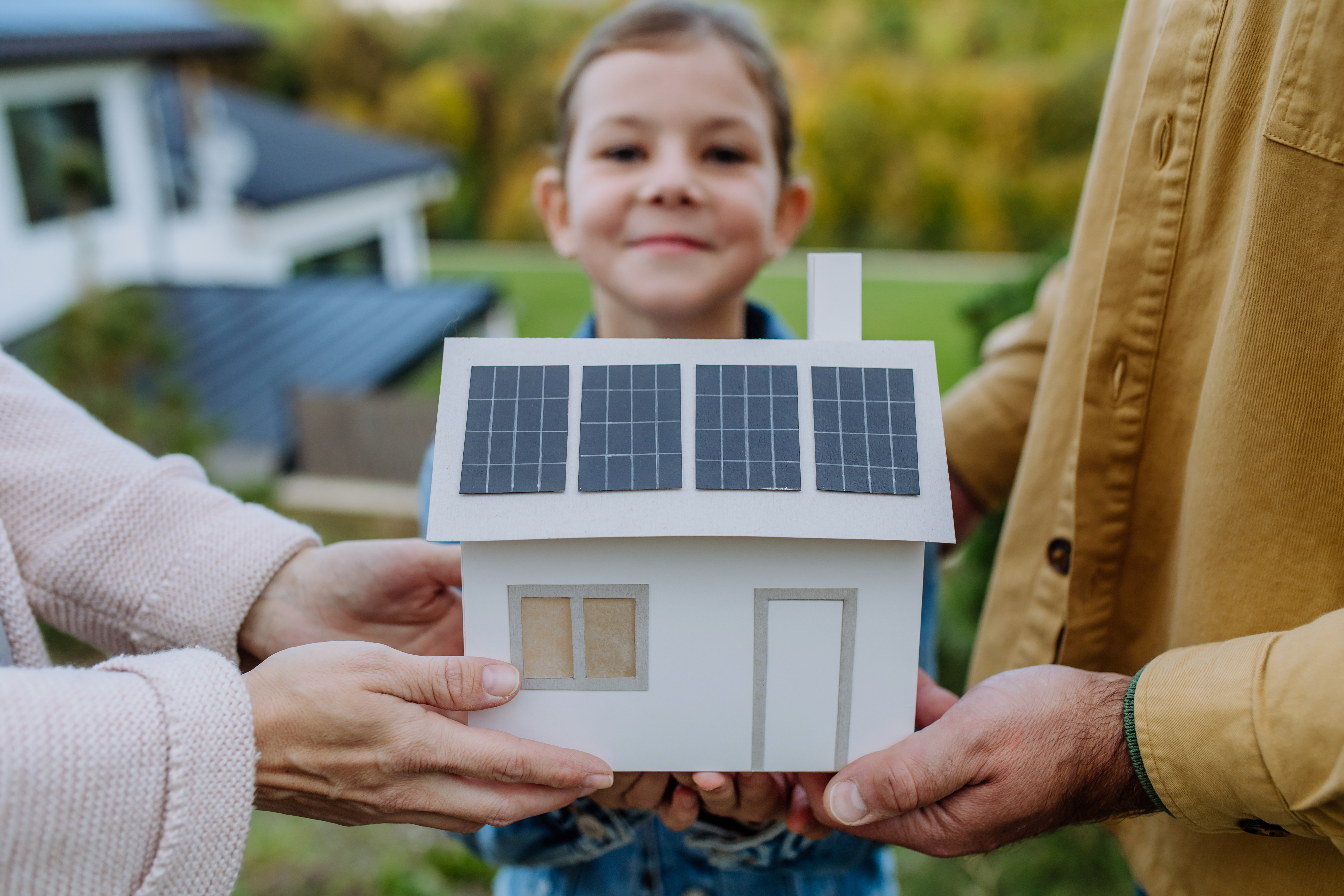 Kind und Eltern halten Modellhaus mit Photovoltaik