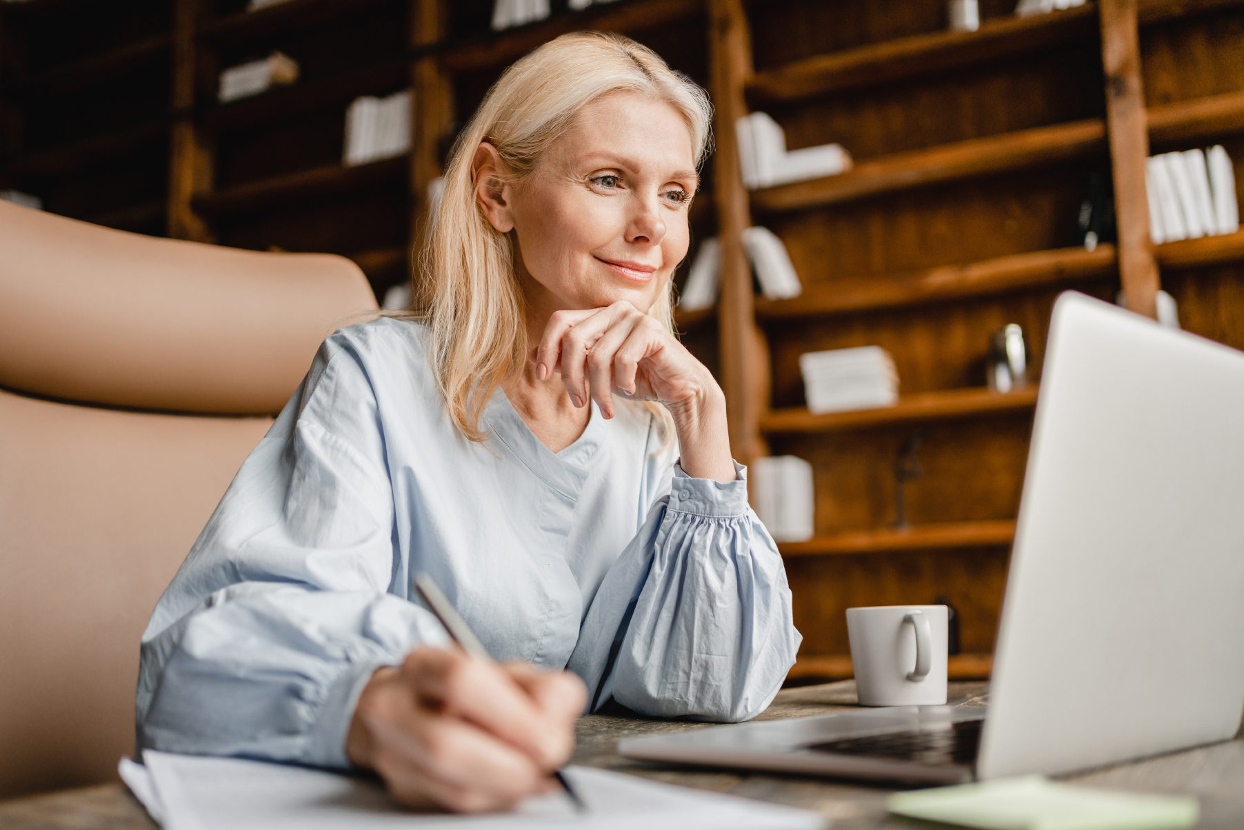 Frau im Home-Office sitzt vor Laptop und macht sich Notizen